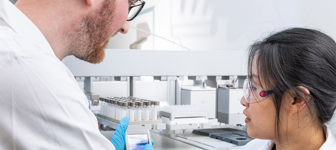 Two scientists working together in a lab, discussing data beside a PAL System automated workstation